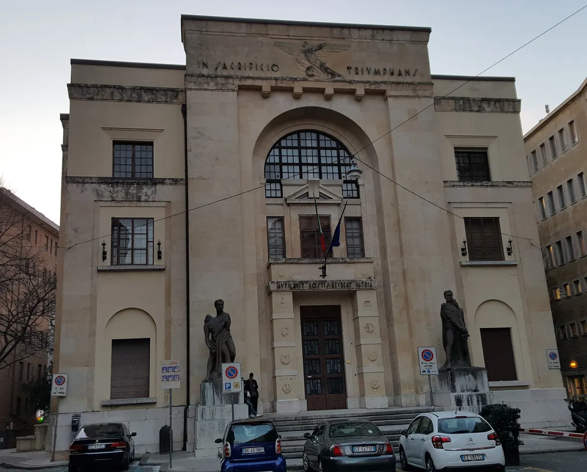 The stone front of the palace on via dei Mutilati, with a large arched window above the door and a statue on each side