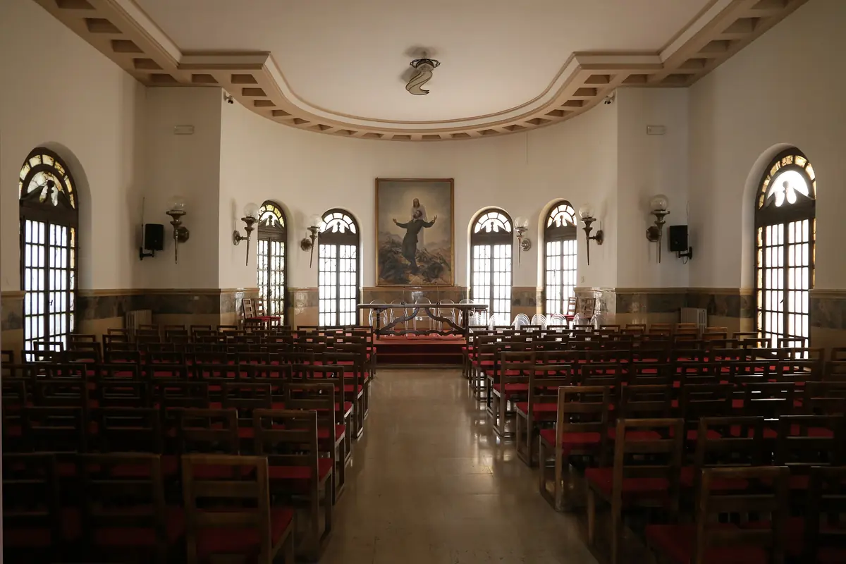 The Sala Antonio Girelli, with rows of wooden chairs facing a curved apse with arched windows and a painting